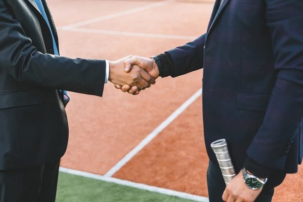 Business handshake. Two businessmen shaking hands while standing outdoors holding tennis rackets. Men shaking hands during a meeting on outdoors background, success, dealing, greeting and partner.